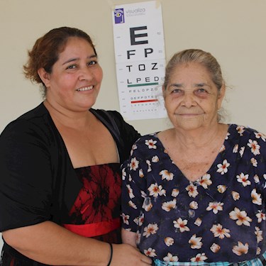 Two women stand in front of an eye chart